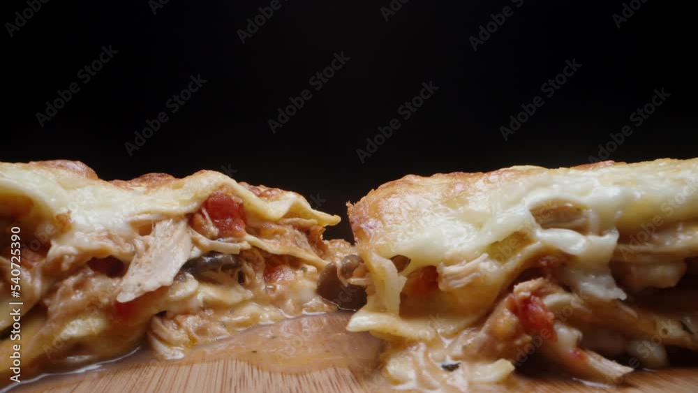 Two pieces of lasagna on a wooden table. Black background, close-up. Two pieces of lasagna on a wooden table. Black background, close-up.