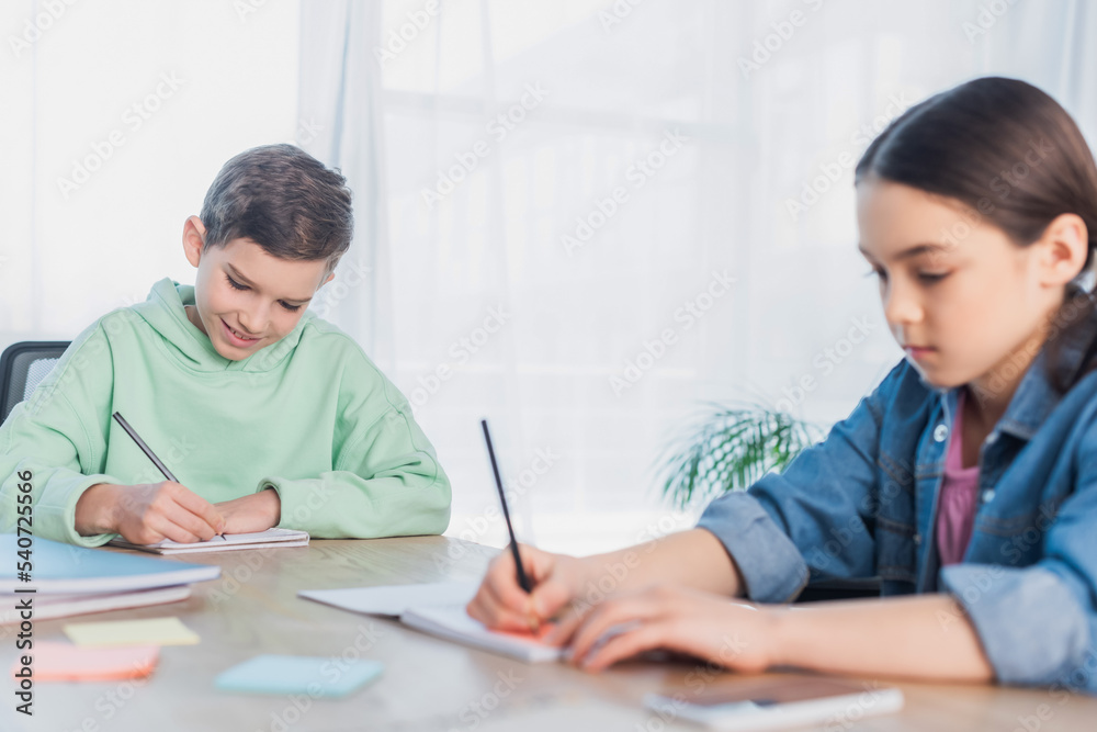 preteen kids writing in notebooks while doing homework on blurred foreground. preteen kids writing in notebooks while doing homework on blurred foreground.