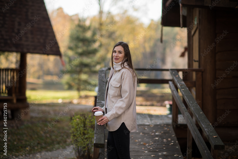 Young happy woman relaxing with hot tea or coffee on the cozy terrace of a wooden country house. Autumn cozy day.