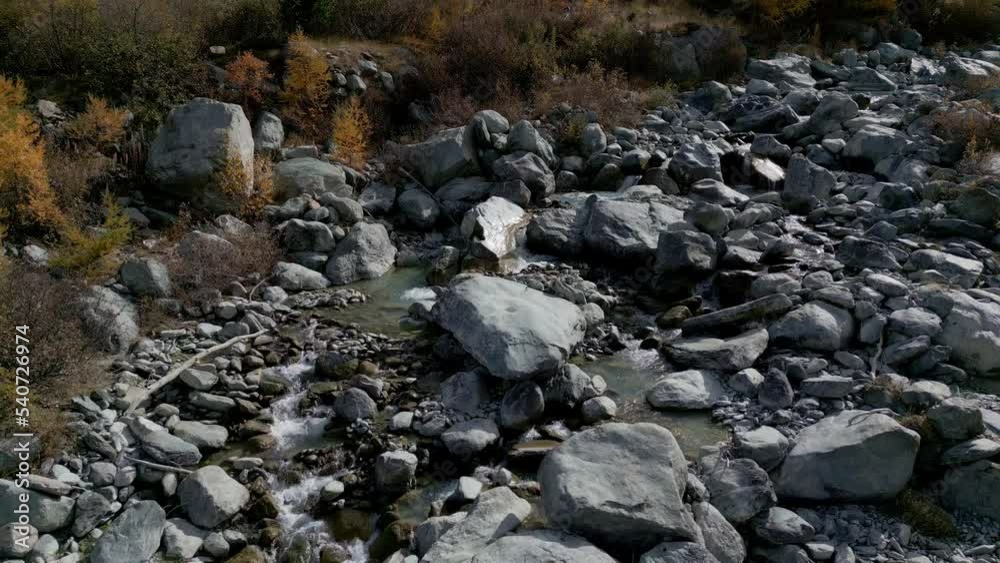 A stream bed in the middle of the Swiss Alps. Many stones lie around and the trees are in autumn colors. Steady Aerial Shot A stream bed in the middle of the Swiss Alps. Many stones lie around and the trees are in autumn colors. Steady Aerial Shot