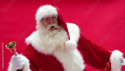 Happy Santa Claus ringing a golden bell on the red studio background. Xmas time. Christmas vibes.