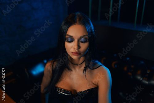 A sexy and beautiful woman enjoys a hookah in a nightclub. Glamorous clothes and neon lights.