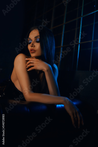 A sexy and beautiful woman enjoys a hookah in a nightclub. Glamorous clothes and neon lights.