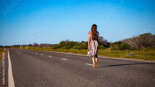 a beautiful long-haired girl in a long dress walks along a road in the desert in western australia  a beautiful girl lost in the middle of nowhere in the australian outback