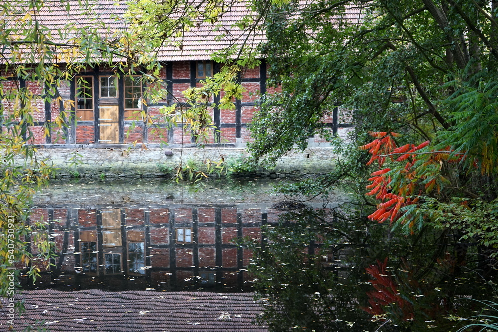 Spiegelung eines schönen alten Fachwerkhaus vom Kleinen Teich am alten Meierhof Heepen am Leithenhof an der Lutter im Herbst in Bielefeld im Teutoburger Wald in Ostwestfalen-Lippe - obrazy, fototapety, plakaty 