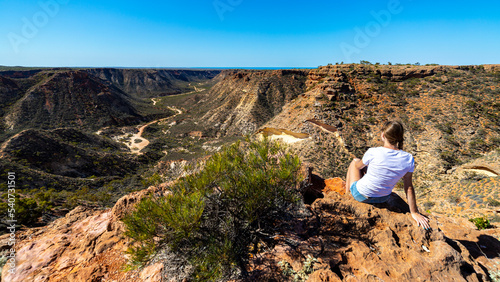 a long-haired girl sits on the edge of a gorge in cape range national park near exmouth in western australia, hiking in the wilderness of western australia