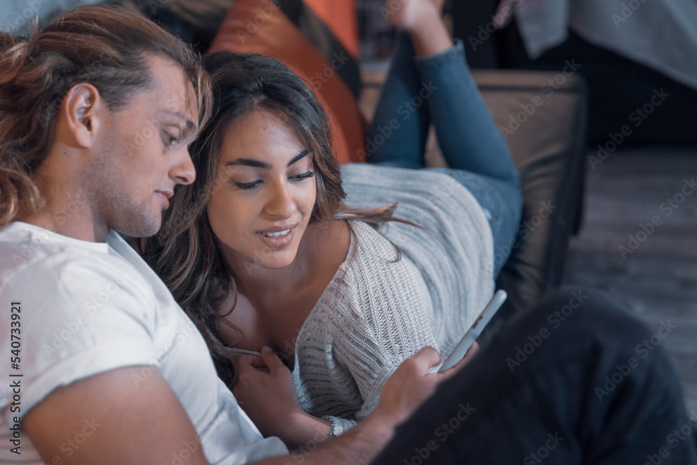 Cheerful couple of romantic caucasian guys smile sharing a night message in living room searching and messaging watching their cellphone device. Male fun guy enjoyng his life looking a smart girl Cheerful couple of romantic caucasian guys smile sharing a night message in living room searching and messaging watching their cellphone device. Male fun guy enjoyng his life looking a smart girl