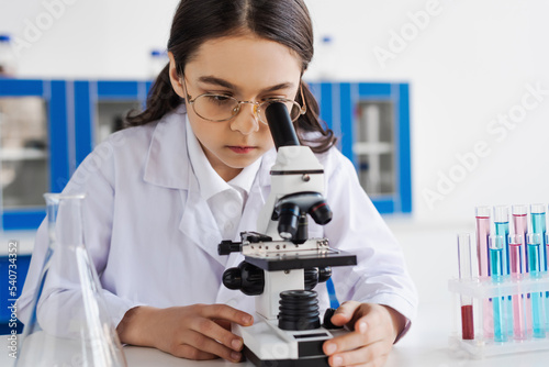 brunette girl in white coat and eyeglasses using microscope in lab.