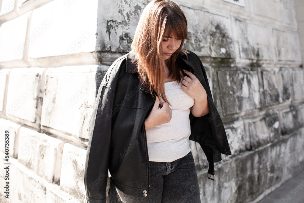 Plus size woman dressed jacket, jeans and t-shirt posing against wall in the street Plus size woman dressed jacket, jeans and t-shirt posing against wall in the street