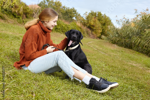 a joyful woman is sitting on the grass with her Labrador retriever dog and enjoying an autumn vacation