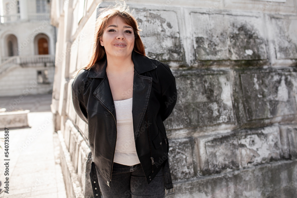 Plus size woman dressed jacket, jeans and t-shirt posing against wall in the street Plus size woman dressed jacket, jeans and t-shirt posing against wall in the street