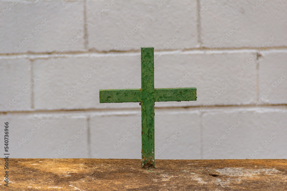 Uma cruz verde com uma parede branca de tijolos ao fundo. 