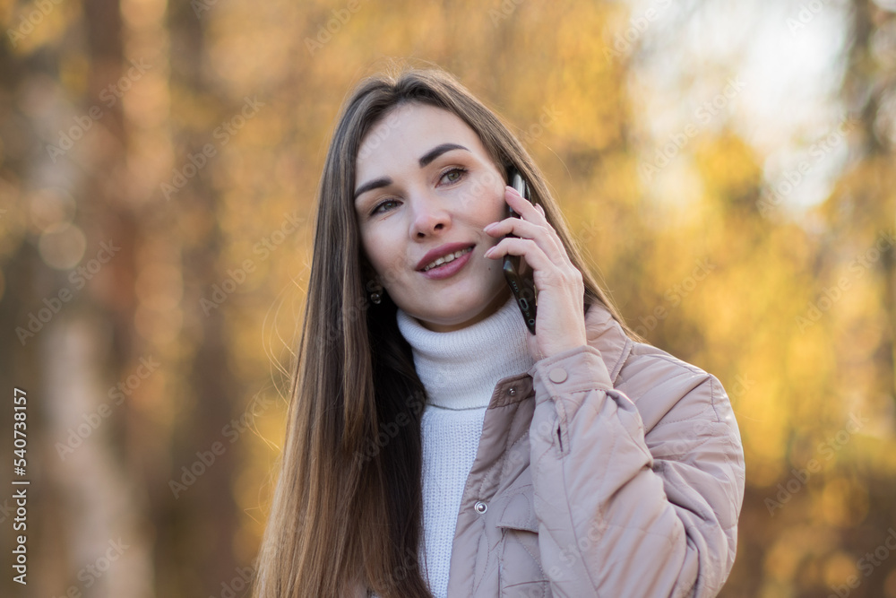 close-up portrait of a young girl with a mobile phone, the girl is talking on the phone against the background of yellow foliage close-up portrait of a young girl with a mobile phone, the girl is talking on the phone against the background of yellow foliage