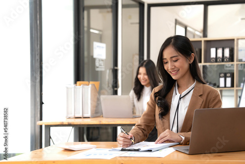 Asian Business woman using calculator and laptop for doing math finance on an office desk, tax, report, accounting, statistics, and analytical research concept