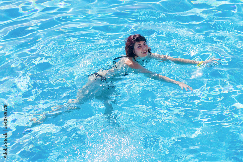 Young brunette woman swims in the blue water of the pool.