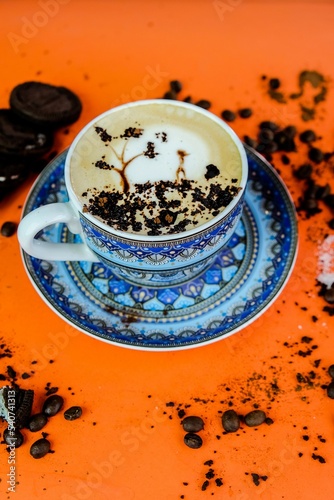 Vertical shot of a Cappuccino with art on an orange table with cookies