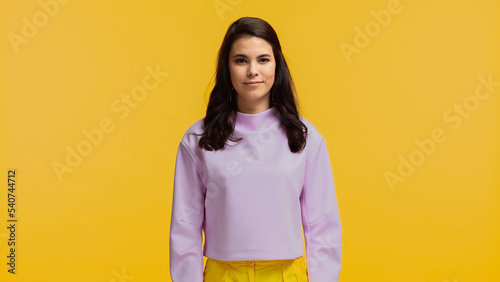 brunette woman in purple sweatshirt standing and looking at camera isolated on yellow © LIGHTFIELD STUDIOS