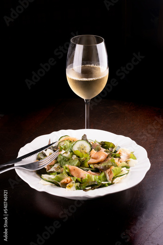 Salad plates with cucumber and salmon on wooden table healthy eating with glass of green white wine top view with fork and knife