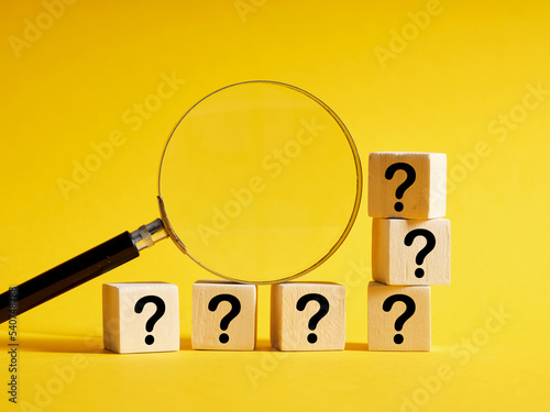 Magnifying glass with wooden cubes with question marks.