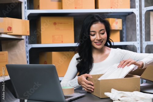 A young business owner is happily checking orders from a laptop to prepare them for delivery to customers. E-commerce business is selling products on the Internet. © Wasaphol