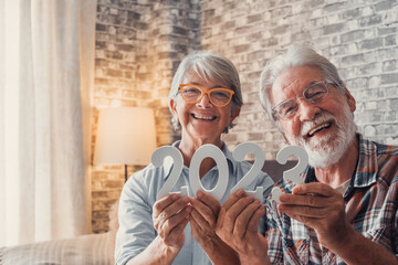 Portrait of couple of two old pensioners holding together numbers of 2023 at home. Close up of new year numbers, celebrating and goals for new life concept.