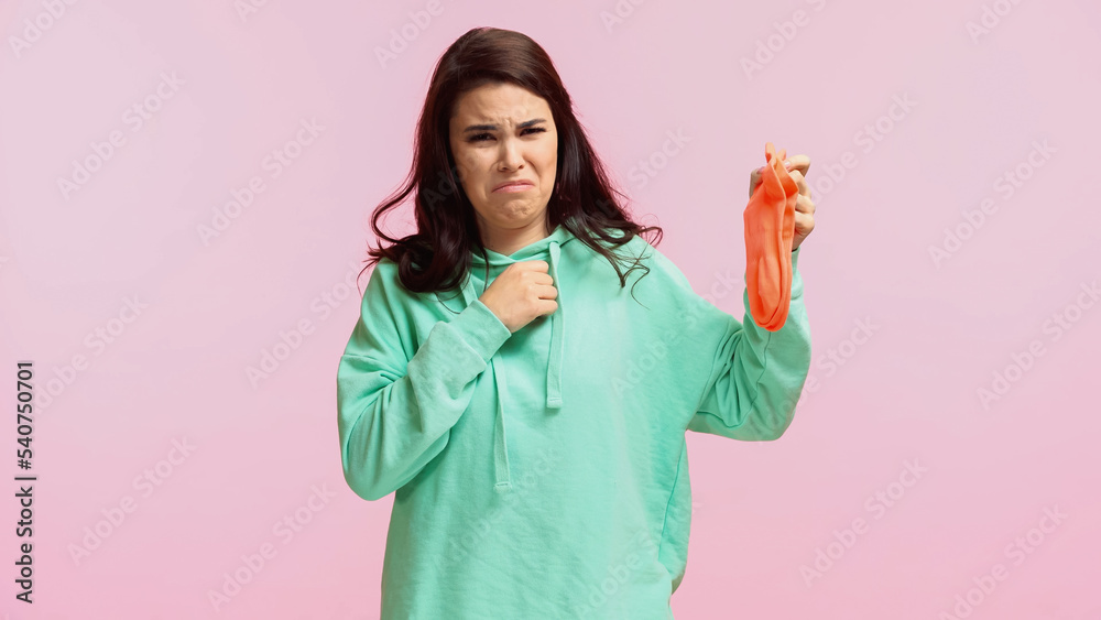 young and disgusted woman in turquoise hoodie holding stinky socks isolated on pink young and disgusted woman in turquoise hoodie holding stinky socks isolated on pink