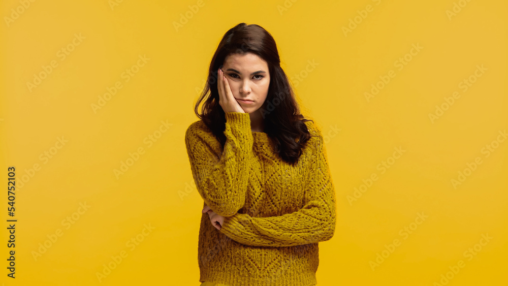 young and bored woman in sweater touching cheek isolated on yellow young and bored woman in sweater touching cheek isolated on yellow