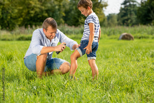 Father applying insect repellent on his son in park photo