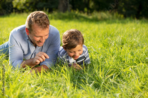 Father and son watching bugs in the grass using magnifying glass