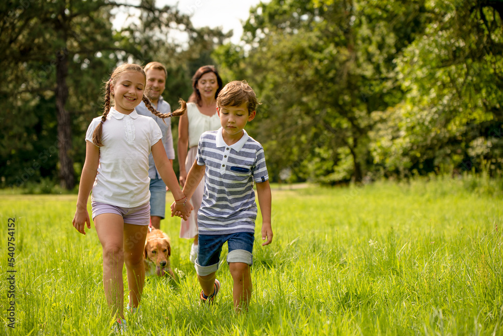 Authentic siblings spending time with their parents walking in park Authentic siblings spending time with their parents walking in park