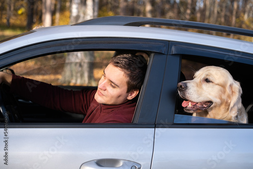 A young man and his dog sit in the car and look out the window. A young man with a golden retriever on a car trip in an autumn forest