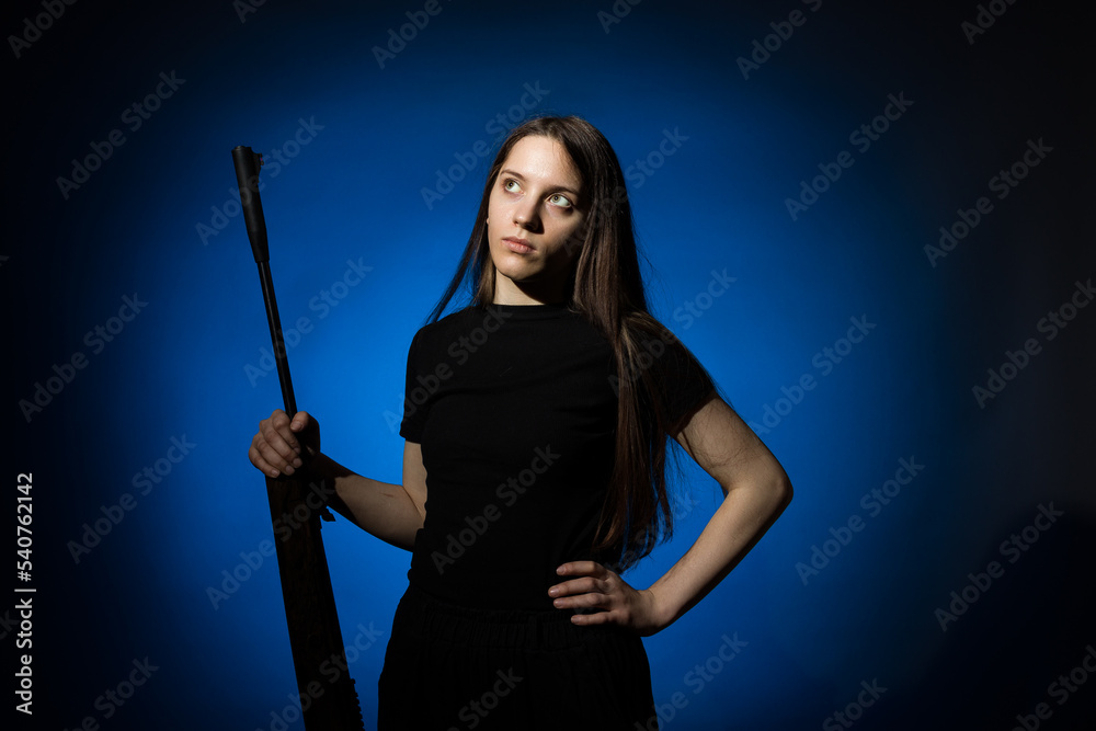 a young girl with long flowing hair in a black T-shirt with a rifle, stands on a dark background a young girl with long flowing hair in a black T-shirt with a rifle, stands on a dark background