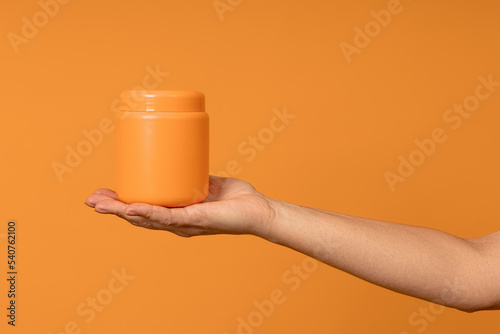 plastic opaque jar of yellow color on a female palm on a yellow background