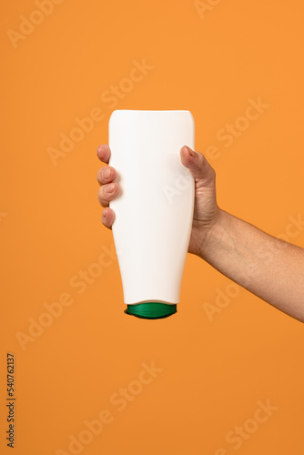 white bottle with a green cap upside down in a hand on a yellow background