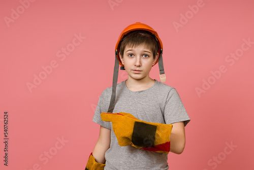 a child in a hard hat and construction gloves points a finger to the side on a pink background