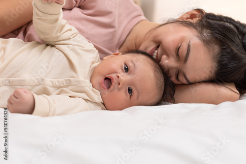 Mom and baby are laying down and cuddling. Mom is kissing her son and both are smiling. Cute baby boy is look so happy and enjoy playing with mom on bed. The baby has chubby and healthy. Good moment