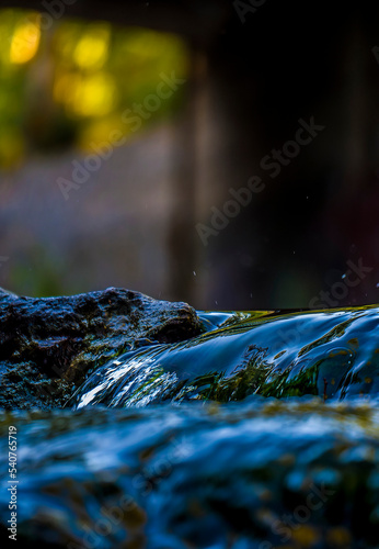 Smooth cascade of a small stream of freshwater. Sunlight creates colorful shades in the background.