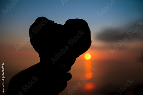 Sea stone in the shape of a heart against with sunset