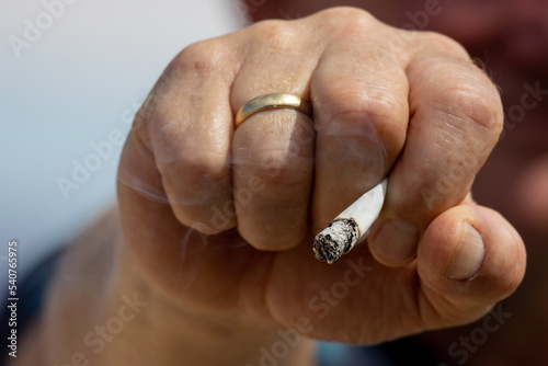 A burning cigarette with cigarette smoke in a male hand, addictive and dangerous to health