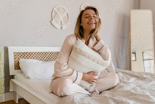 pretty smiling woman relaxing at home on bed in morning in pajamas photo
