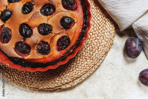 Fresh homemade plum pie in ceramic form on grey concrete background. Plum Skillet Cake. Delicious summer dessert. Selective focus