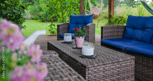 Natural cozy covered terrace with green nature in summer. Rattan and wicker furniture with cushions, flowers and plant outdoor. Relax in patio outdoor.	Banner.