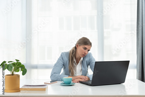 Young frustrated business woman office worker trying to concentrate for her work while she sitting in the company office with old laptop computer and slow internet connection. photo