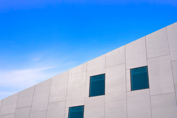 Low angle and side view of glass windows on modern white concrete building wall against blue sky, street style and minimal exterior architecture background