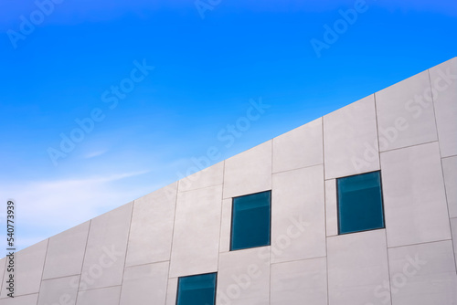 Low angle and side view of glass windows on modern white concrete building wall against blue sky, street style and minimal exterior architecture background