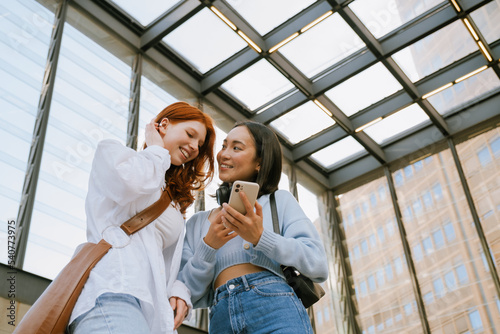 Young multinational women smiling and using cellphone indoors