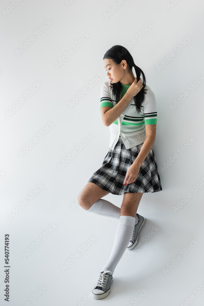 Full length of young asian woman in cropped cardigan and skirt standing on grey background