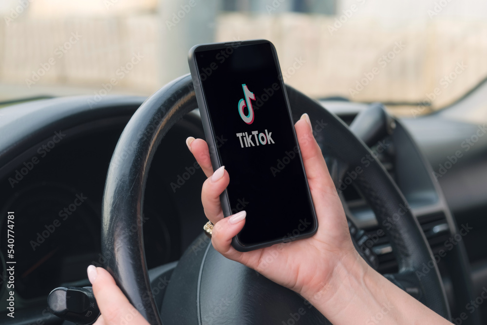 Foto Stock Woman holds a smartphone with Tik Tok app on screen in front of the steering wheel of