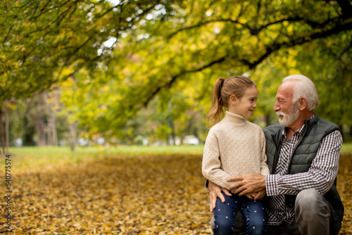 Grandfather spending time with his granddaughter in park on autumn day