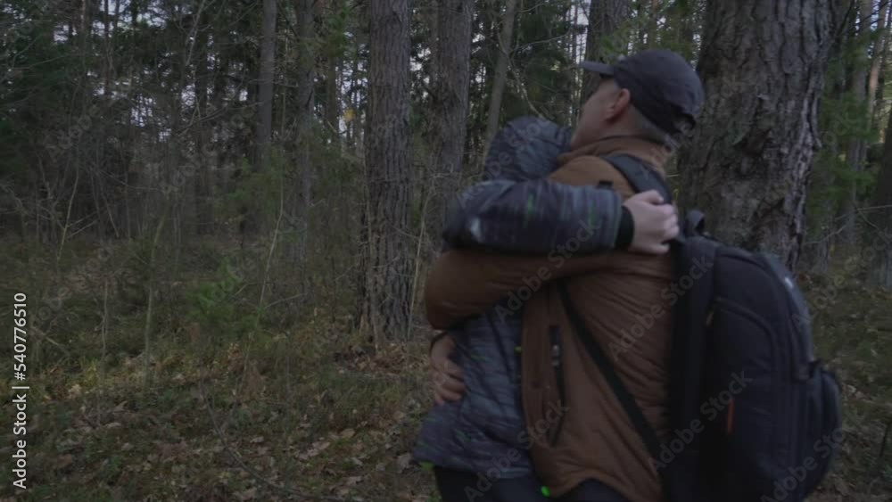 Happy teenager boy embracing with him smiling father in forest. Dad and son rejoice at meeting after separation.